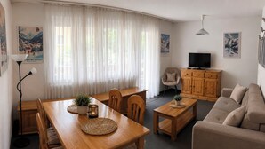Ein möbliertes Wohnzimmer mit Esstisch, Sofa und Fernseher.