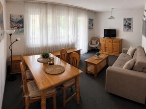 A furnished living room with a dining table, sofa, and television. - Majesta Leukerbad # 4-bed apartment, Dusche, WC by Interhome (Leukerbad)