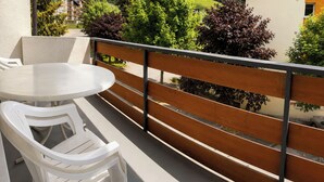 Ein Balkon mit rundem Tisch und zwei Stühlen, mit Blick auf eine gebirgige Landschaft mit Bäumen und einem Gebäude.