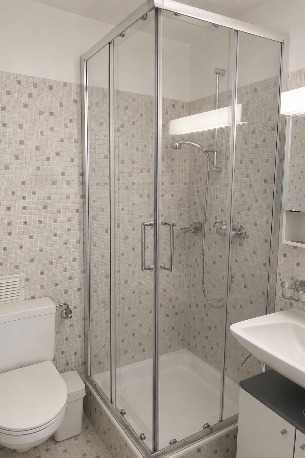 Une salle de bain moderne avec une douche à parois de verre, des toilettes blanches et un lavabo avec un miroir.