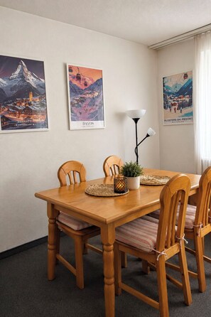 A dining area with a wooden table, four chairs, a lamp, and three framed posters on the wall. - Majesta Leukerbad # 4-bed apartment, Dusche, WC by Interhome (Leukerbad)