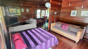 A wooden interior with a sofa, a bed with a striped bedspread, and a fan. - Costa Rican Paradise (La fortuna)