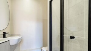 A modern bathroom with a white sink, a toilet, and a glass shower enclosure. - Shore Thing - Relaxing Sea View Getaway (Portsmouth)