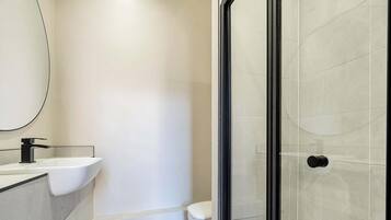 Un baño moderno con un lavamanos blanco, un inodoro y una cabina de ducha con paredes de vidrio.