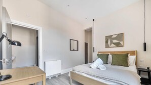 A bedroom with a bed, bedside table, lamp, radiator, and a framed picture on the wall. - Shore Thing - Relaxing Sea View Getaway (Portsmouth)