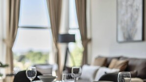 A dining area with a table set for two, a sofa in the background, and a window with curtains. - Shore Thing - Relaxing Sea View Getaway (Portsmouth)