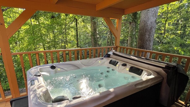 Ein Whirlpool auf einer Holzterrasse mit Holzgeländer, umgeben von Bäumen.