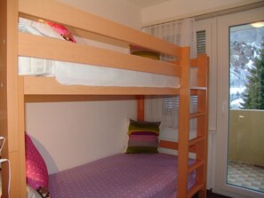 Een slaapkamer met stapelbed, raam en uitzicht op bomen.