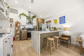 Eine moderne Küche mit einer zentralen Kochinsel, Holzbarhocker und einem Schild mit der Aufschrift 'Cool People Live Here'.