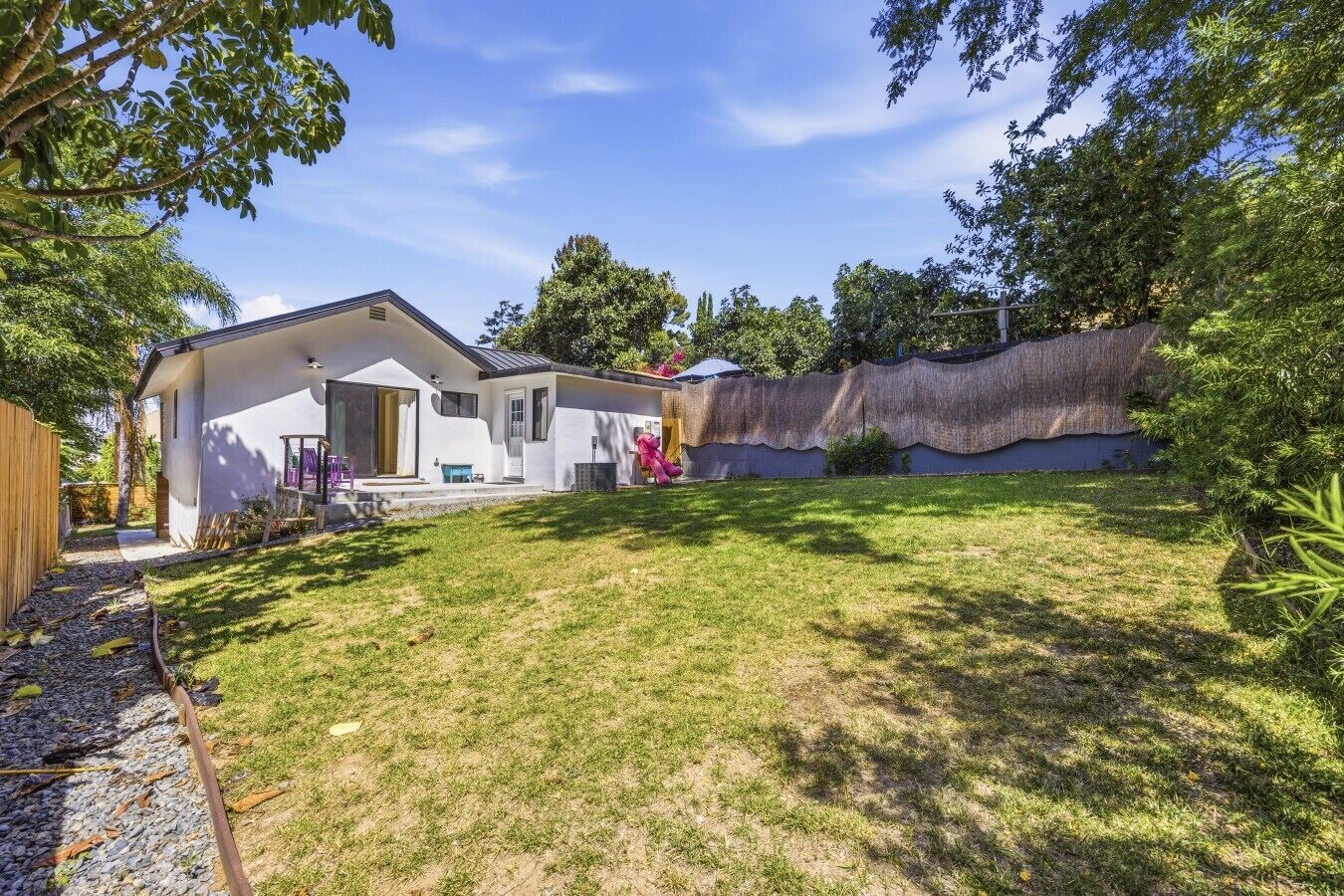 A modern house with a covered patio, a fenced yard, and a thatched wall.