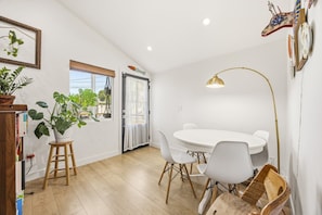 A dining area with a round table, white chairs, a wooden stool, a potted plant, and a floor lamp. - Cozy Highland Park Family Home w/ EV (Los Angeles)