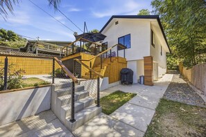 A modern two-story house with a wooden staircase, a barbecue grill, and a small garden area. - Cozy Highland Park Family Home w/ EV (Los Angeles)