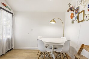 Ein Essbereich mit einem runden Tisch, weißen Stühlen, einer goldenen Stehlampe und einem weißen Vorhang.
