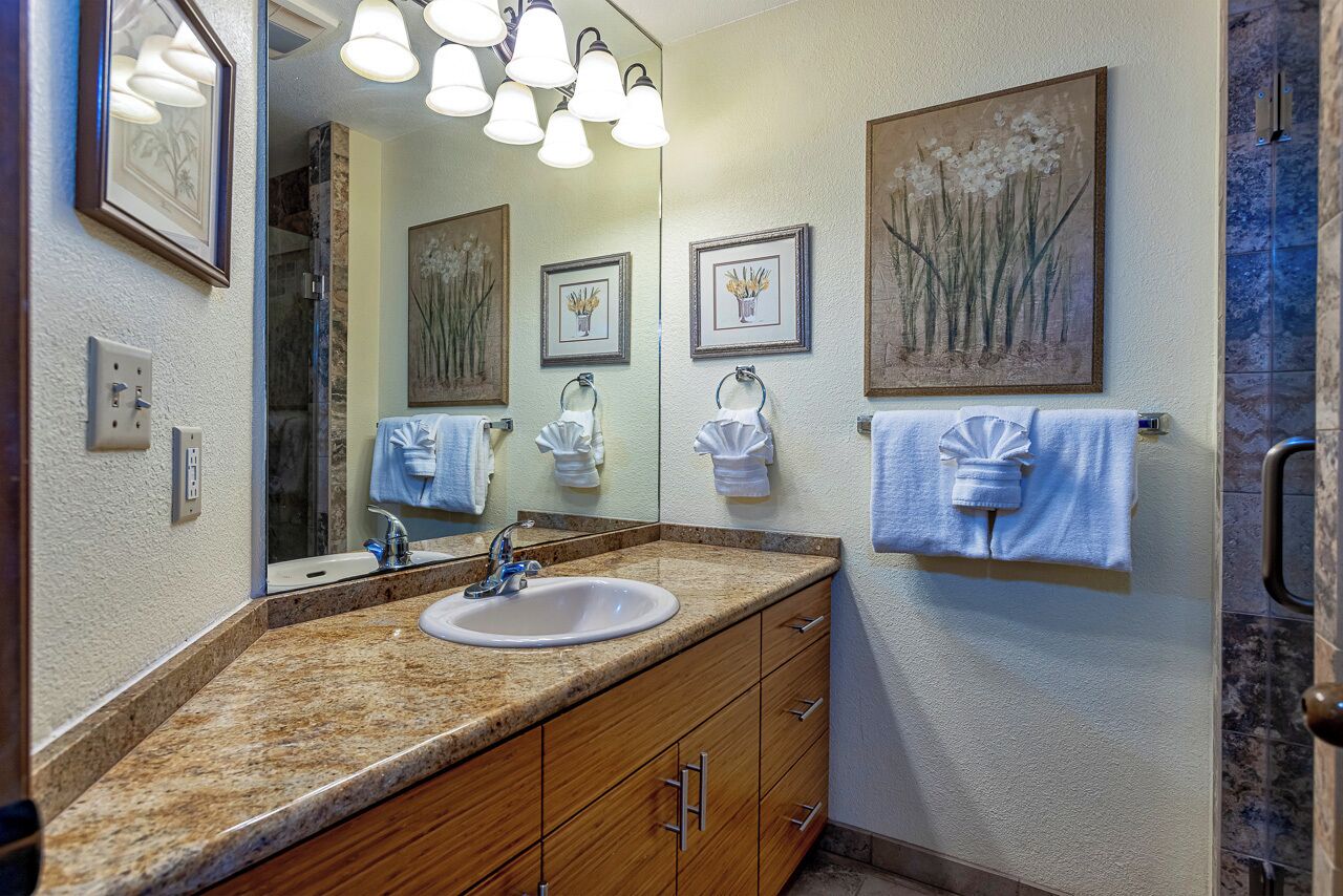 A bathroom with a granite countertop, a sink, a mirror, and framed artwork on the wall.