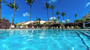 Ein Schwimmbecken mit Liegestühlen, Palmen und Hotelgebäuden.
