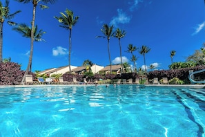 Ein Schwimmbecken mit Liegestühlen, Palmen und Hotelgebäuden.