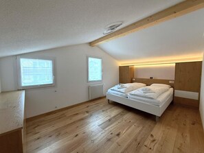Una habitación pequeña con cama individual, piso de madera, paredes blancas y techo inclinado.