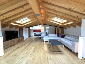 A spacious loft with a high ceiling, wooden beams, a large TV, a sofa, a dining table, and a kitchen area. - Diana 9 # 3-bed apartment, Dusche, WC 3-Bettwohnung, Dusche, WC by Interhome (Leukerbad)