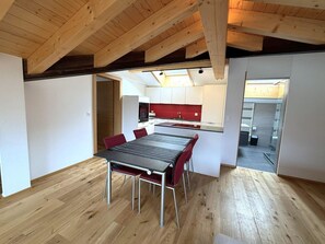 A modern kitchen with white cabinets and a red backsplash, a dining area with a black table and red chairs, and a wooden ceiling with exposed beams. - Diana 9 # 3-bed apartment, Dusche, WC 3-Bettwohnung, Dusche, WC by Interhome (Leukerbad)