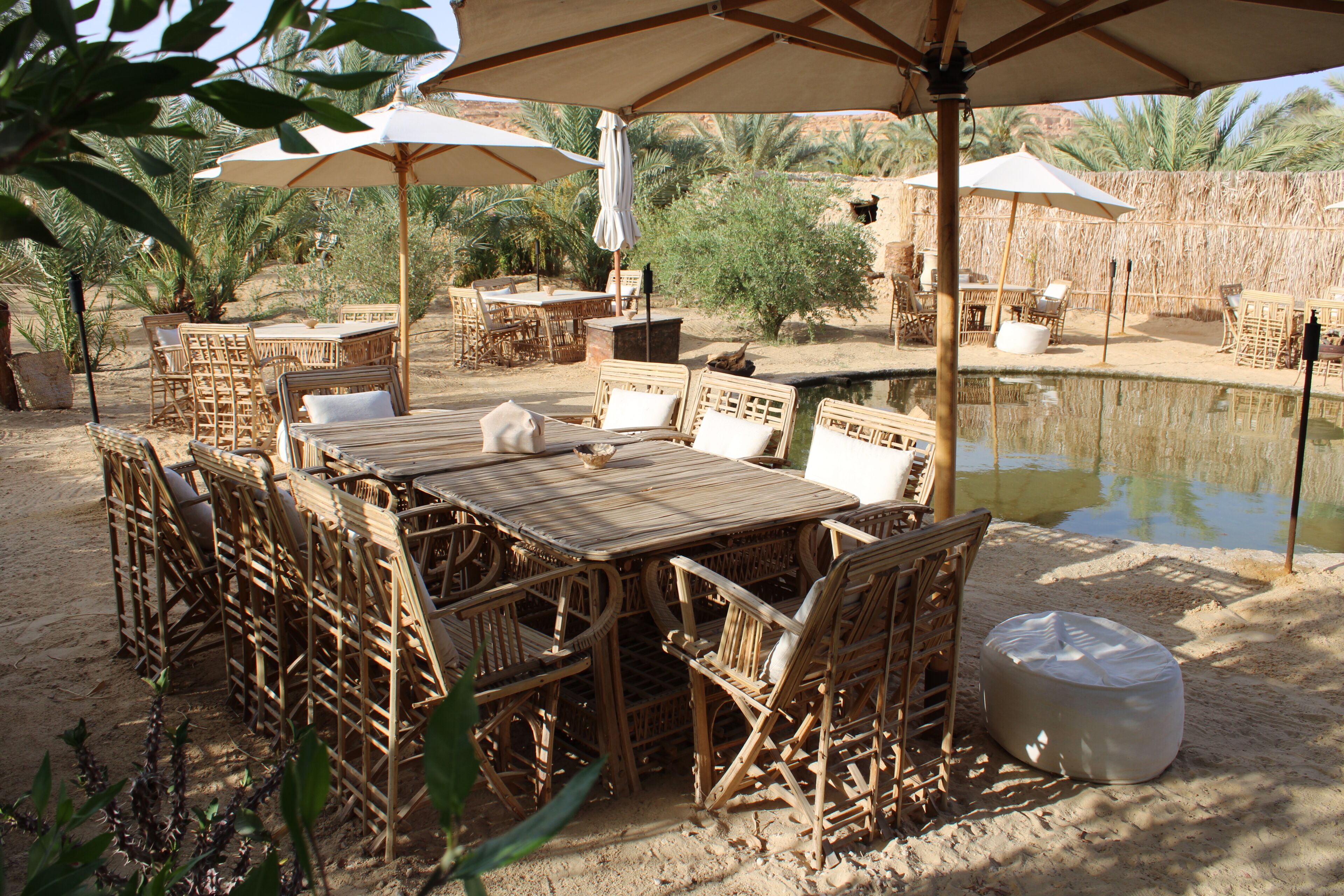 Zona pranzo all'aperto con mobili in vimini, ombrelloni e una piccola piscina.