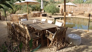 An outdoor dining area with wicker furniture, umbrellas, and a small pool. - tanirt ecolodge (Siwa)