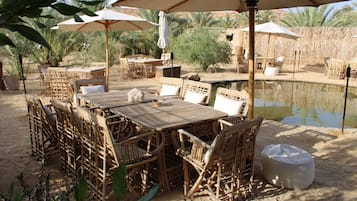 Zona pranzo all'aperto con mobili in vimini, ombrelloni e una piccola piscina.