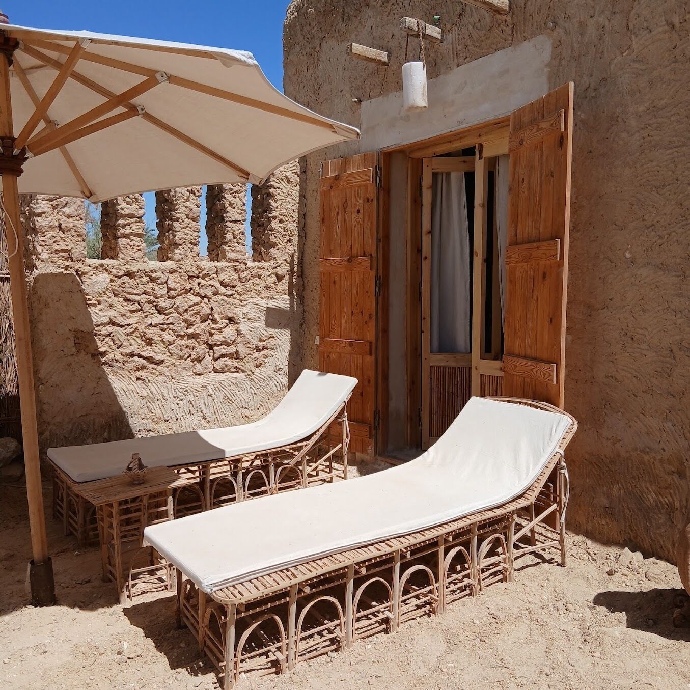 A wooden outdoor seating area with two lounge chairs and a table, a wooden door, and a stone wall.