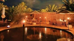 A nighttime outdoor pool area with a fire, lounge chairs, and umbrellas. - tanirt ecolodge (Siwa)