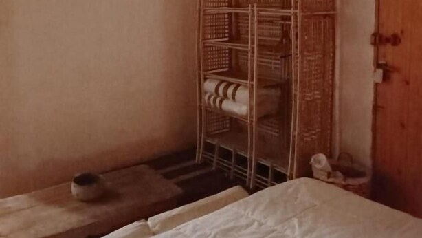 A room with a bed, a wooden cabinet, and a metal rack with folded items. - tanirt ecolodge (Siwa)