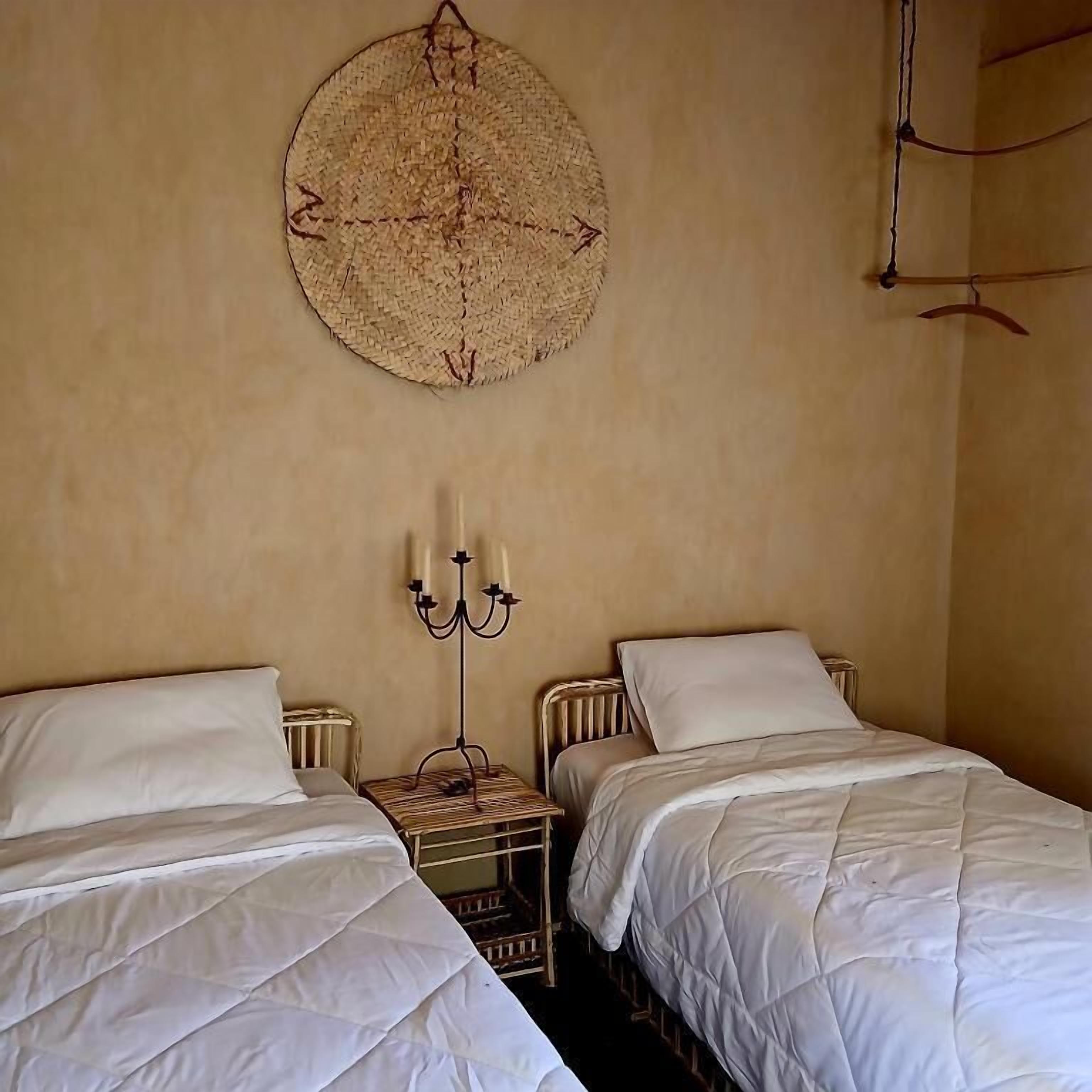 Ein Schlafzimmer mit zwei Einzelbetten, einem wandmontierten, runden Gewebekunstwerk und einem Kandelaber.