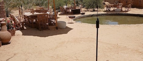 An outdoor seating area with tables and chairs, umbrellas, and a small pool.