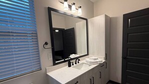 A bathroom with a white sink, black faucet, and a large mirror above it. There are wooden cabinets below the mirror and a toilet to the left. - Upscale 3BR Townhome Near the World Cup • Sleeps 8 (Decatur)