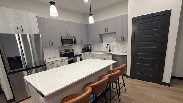 A modern kitchen with a central island, bar stools, stainless steel appliances, and a herringbone-patterned backsplash. - Upscale 3BR Townhome Near the World Cup • Sleeps 8 (Decatur)