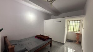 A bedroom with a bed, a ceiling fan, a window with bars, a sink, and a small stool.