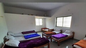 A dormitory room with four beds arranged in a U-shape, a small table, and two windows with bars.