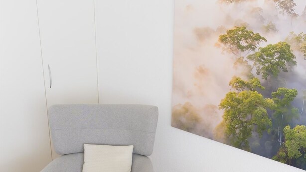Ein Zimmer mit einem grauen Sessel, einem kleinen runden Holztisch und einem großen Wandbild von Bäumen.