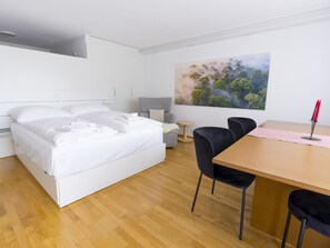 Ein modernes Hotelzimmer mit Bett, Schreibtisch, Stühlen, einem runden Tisch und einem Bild an der Wand.