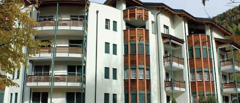 A multi-story building with balconies, a flat roof, and a grassy area in front.