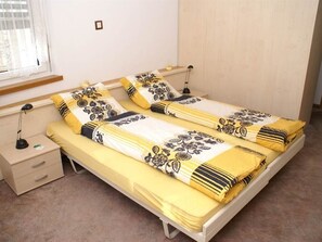 A twin bed with a yellow and white floral bedspread, two bedside tables, a lamp, and a window with curtains. - La Promenade 22 # 2-bed apartment, Dusche, WC 2-Bettwohnung, Dusche, WC by Interhome (Leukerbad)