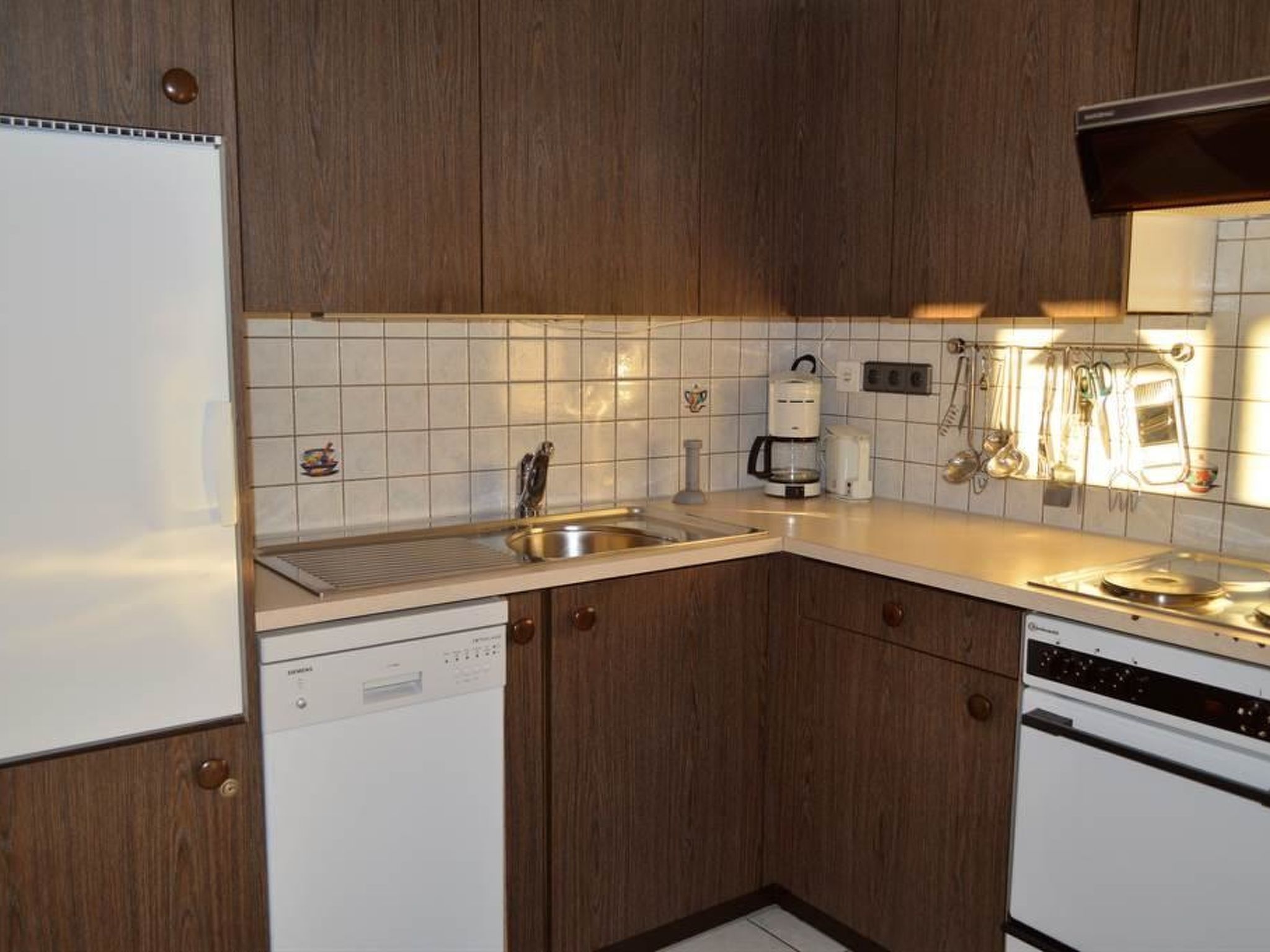 A compact kitchen with wooden cabinets, a white countertop, a built-in dishwasher, a stove, and a coffee maker.