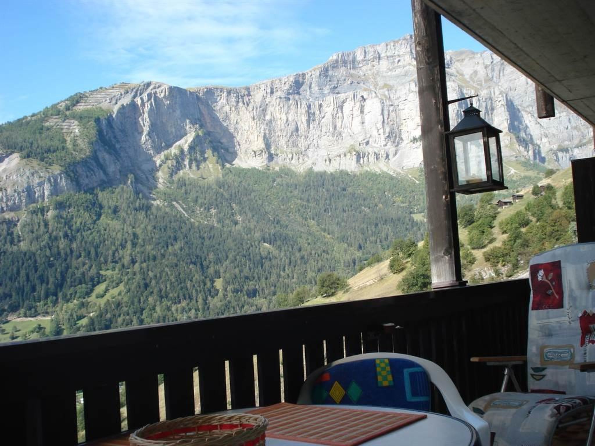 Ein Zimmer mit Blick auf ein Gebirge, ein Tisch mit Unterlage und ein Stuhl mit farbigem Sitzkissen.