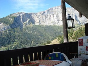 A room with a view of a mountain range, a table with a placemat, and a chair with a colorful cushion. - Albina 43 # 4-bed apartment, Dusche, WC 4-Bettwohnung, Dusche, WC by Interhome (Albinen)