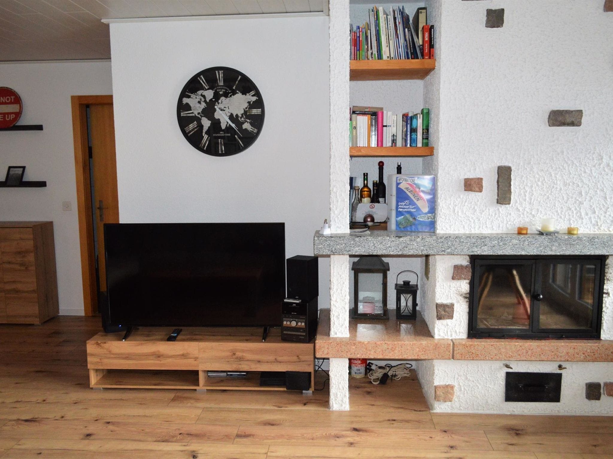 A living room with a flat-screen TV, a world map clock, bookshelves, and a fireplace.
