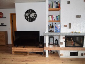 A living room with a flat-screen TV, a world map clock, bookshelves, and a fireplace. - Albina 43 # 4-bed apartment, Dusche, WC 4-Bettwohnung, Dusche, WC by Interhome (Albinen)