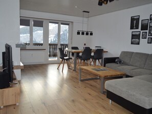 A modern living room with a wooden floor, a grey sofa, a dining table with chairs, and a television on a stand. - Albina 43 # 4-bed apartment, Dusche, WC 4-Bettwohnung, Dusche, WC by Interhome (Albinen)