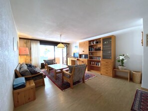 A living room with a sofa, a coffee table, a TV, and a bookshelf. - Lärchenwald 1706 # 6-bed apartment, Dusche, WC 6-Bettwohnung, Dusche, WC by Interhome (Leukerbad)