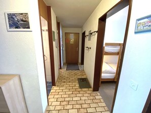 Un couloir avec un sol en briques, des portes en bois et un lit superposé sur le côté droit.
