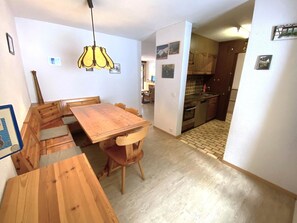 A dining area with a wooden table and chairs, a hanging light fixture, and a kitchen visible through an open doorway. - Lärchenwald 1706 # 6-bed apartment, Dusche, WC 6-Bettwohnung, Dusche, WC by Interhome (Leukerbad)