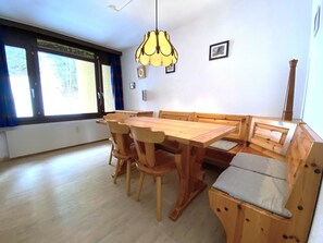 A dining area with a wooden table and chairs, a bench, a hanging light fixture, and a window with curtains. - Lärchenwald 1706 # 6-bed apartment, Dusche, WC 6-Bettwohnung, Dusche, WC by Interhome (Leukerbad)
