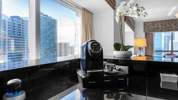 A modern hotel room with a coffee maker, a potted orchid, and a view of the cityscape through large windows.